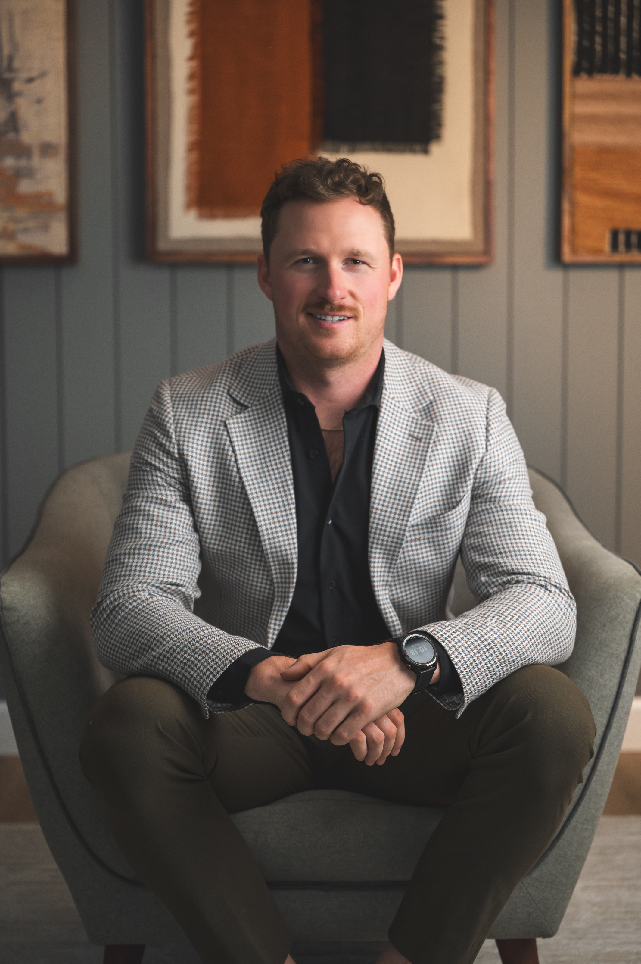Mitch Myers seated in a chair, wearing a checked blazer